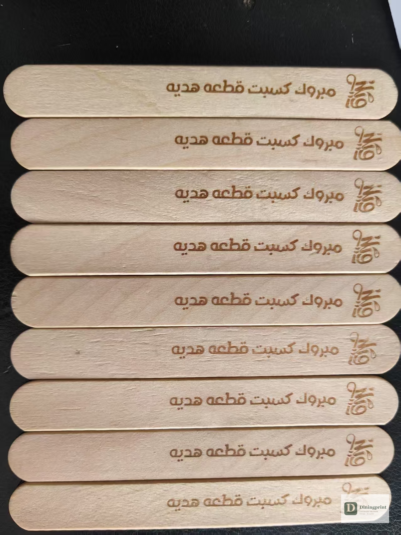 Custom-printed paper-wrapped birchwood sticks with Arabic-language promotional artwork lined up after wrapping