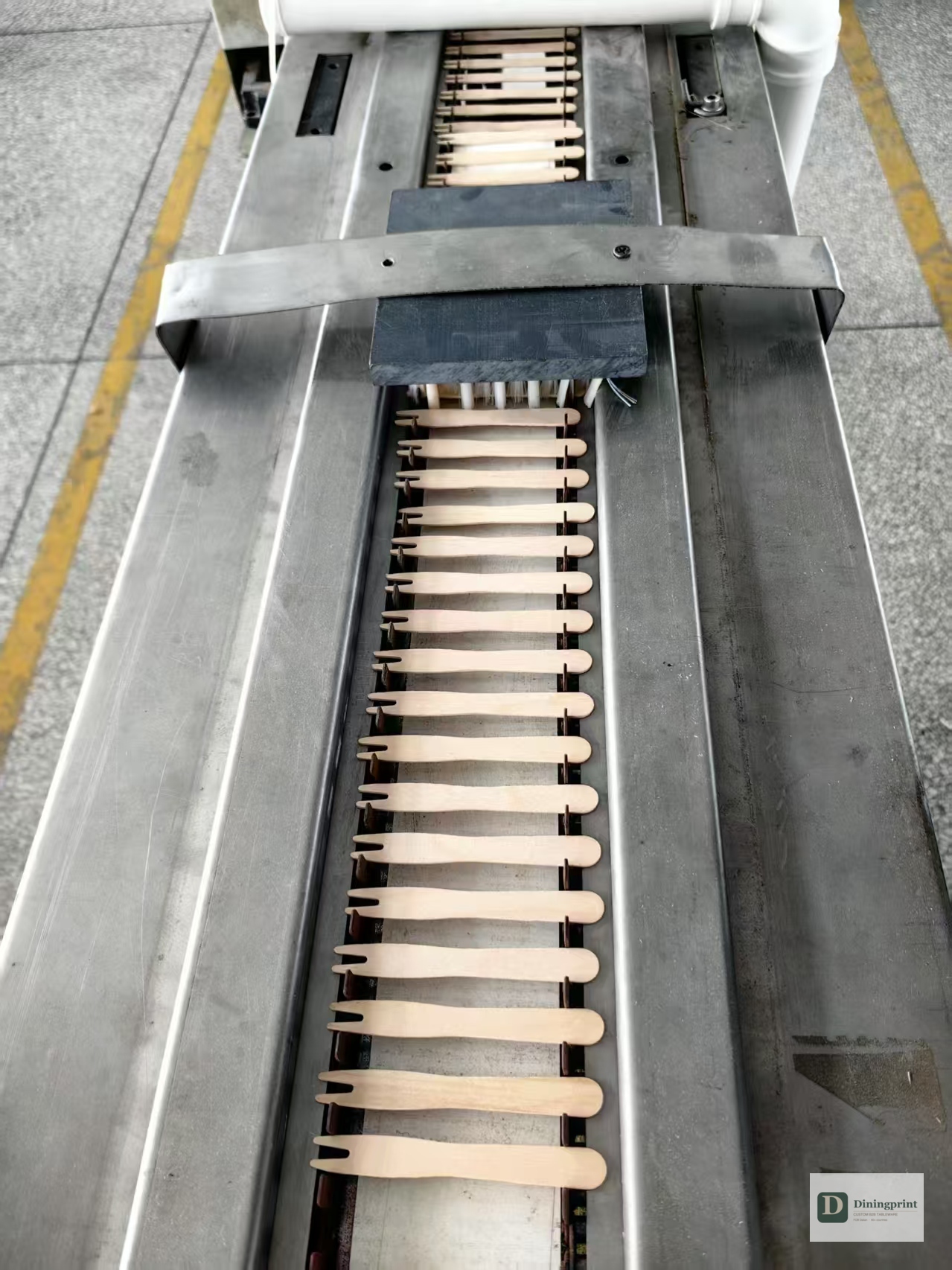 Conveyor belt with rows of wooden cutlery blanks being shaped by overhead pressure heads